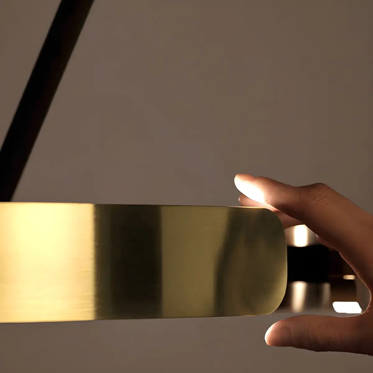 Hand touching the brass-toned LED ring of the floor lamp, close-up detail.