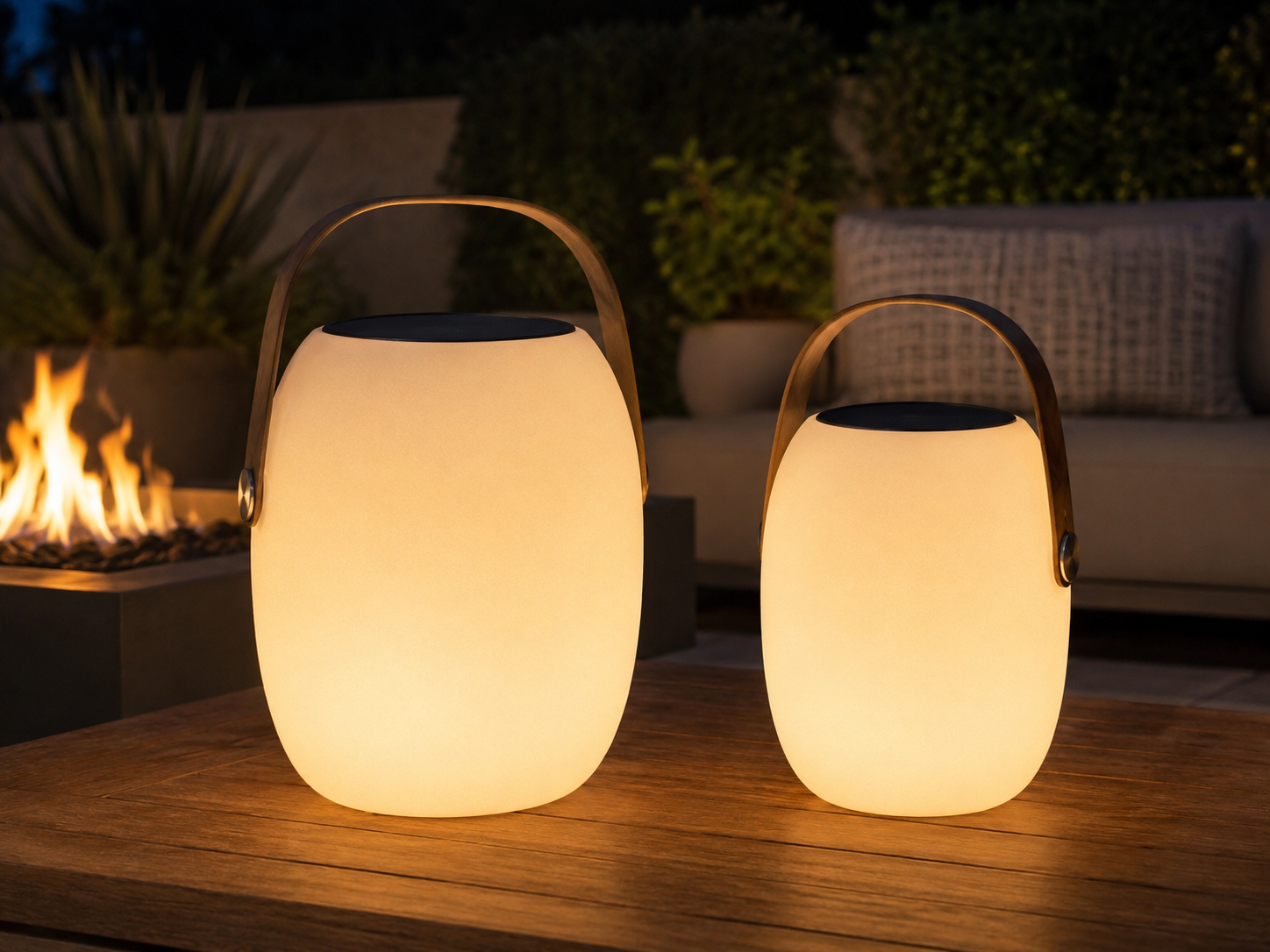 Aire portable outdoor lantern shown in both Small and Large sizes on wood table beside fire pit at night