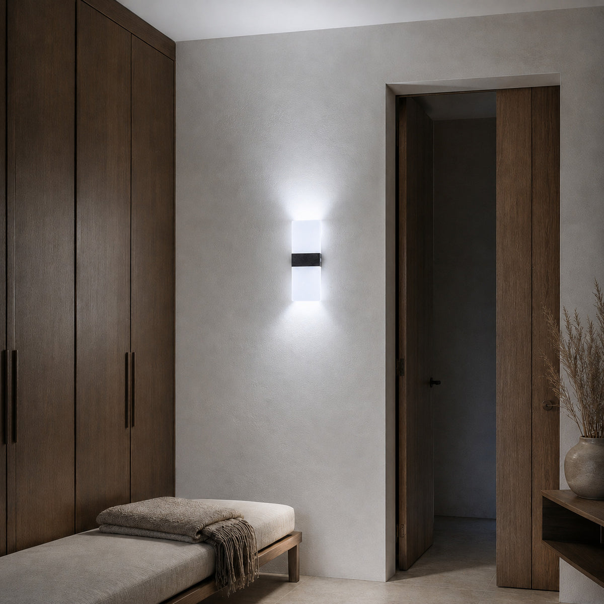 Anços sconce in black with cool white light above a linen bench in a dressing corner