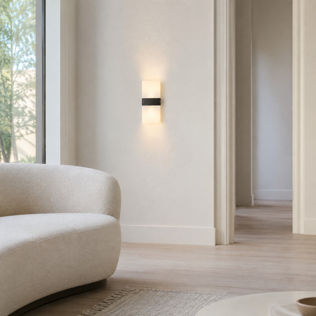 Anços sconce in black with warm white light above a console table in a modern hallway