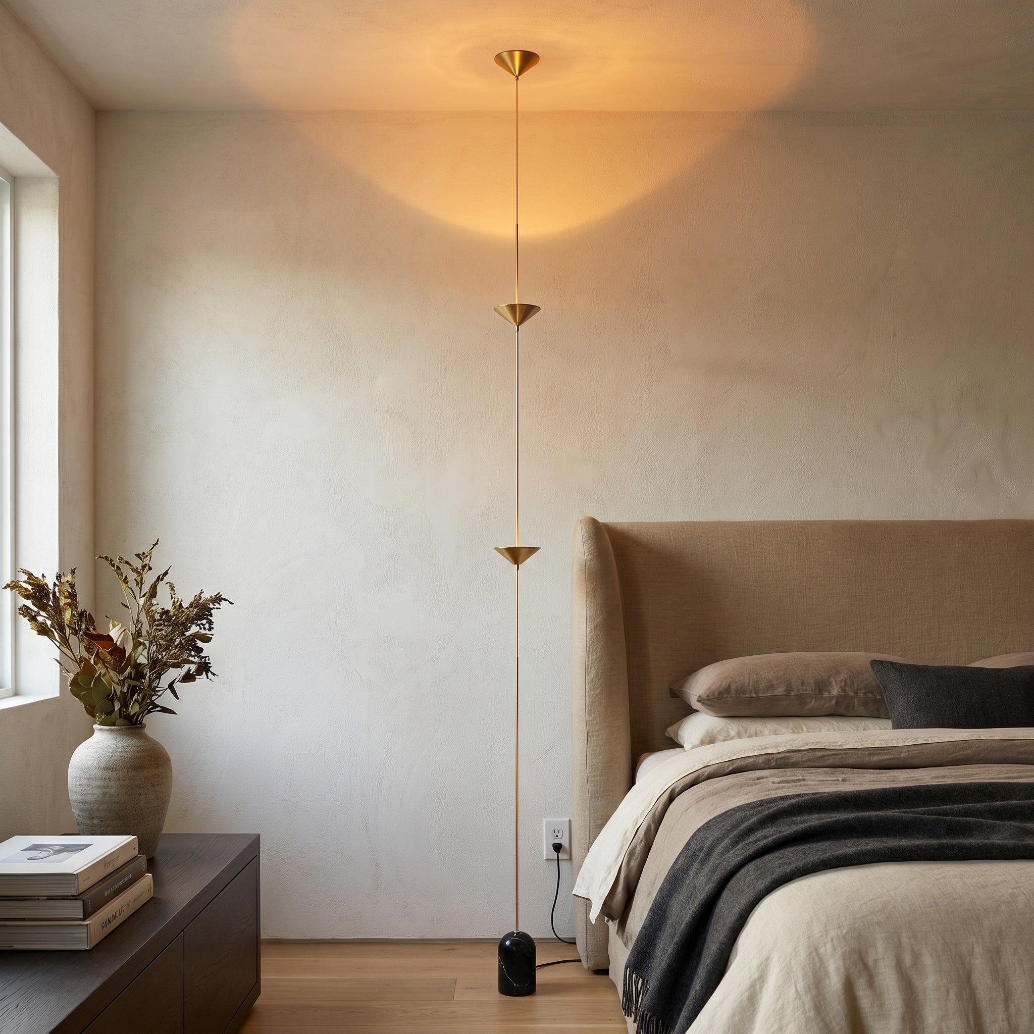 Three-disc gold tension lamp beside a bed with linen bedding and an arched window.