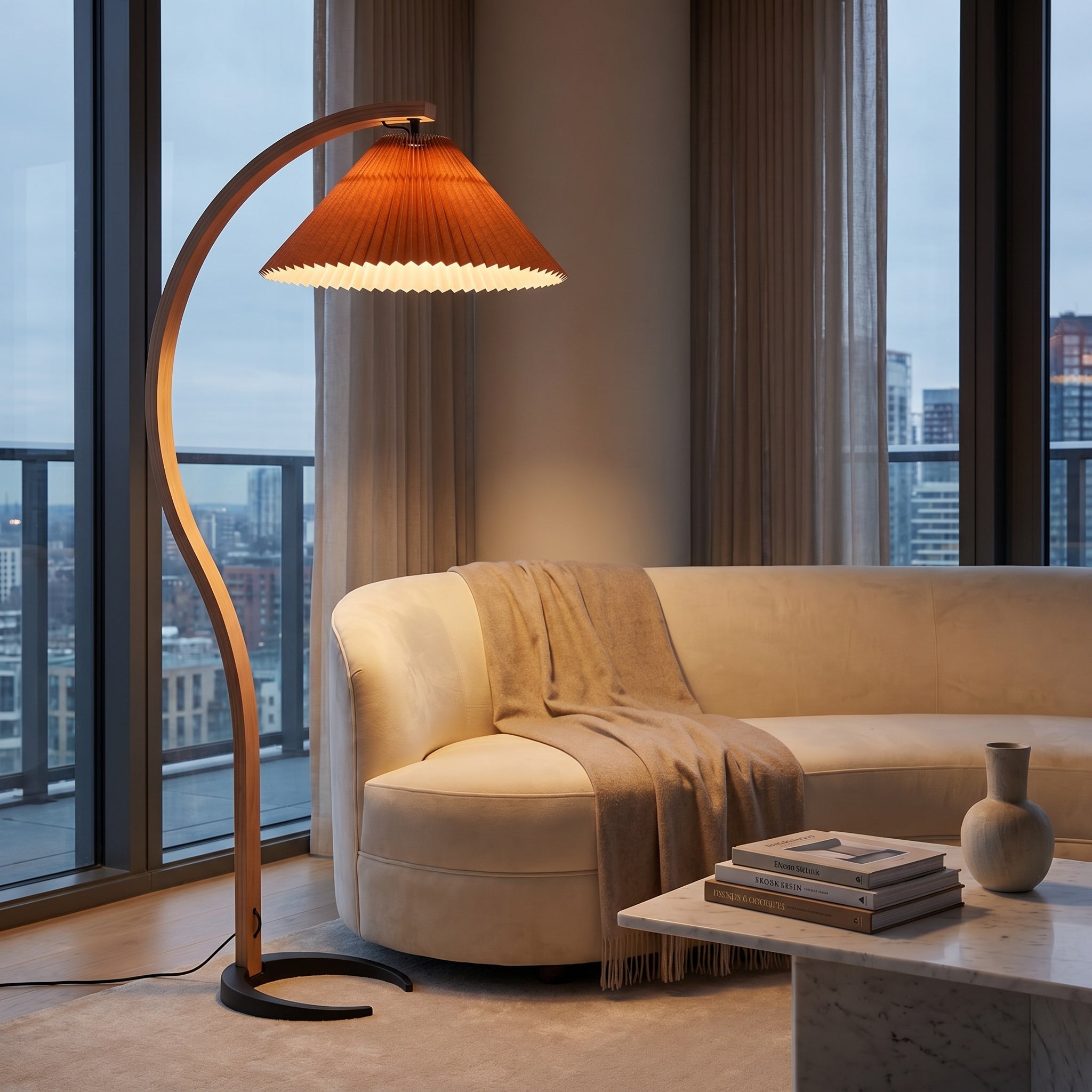 Bentwood beech floor lamp with coffee pleated shade above a beige sectional and city window.