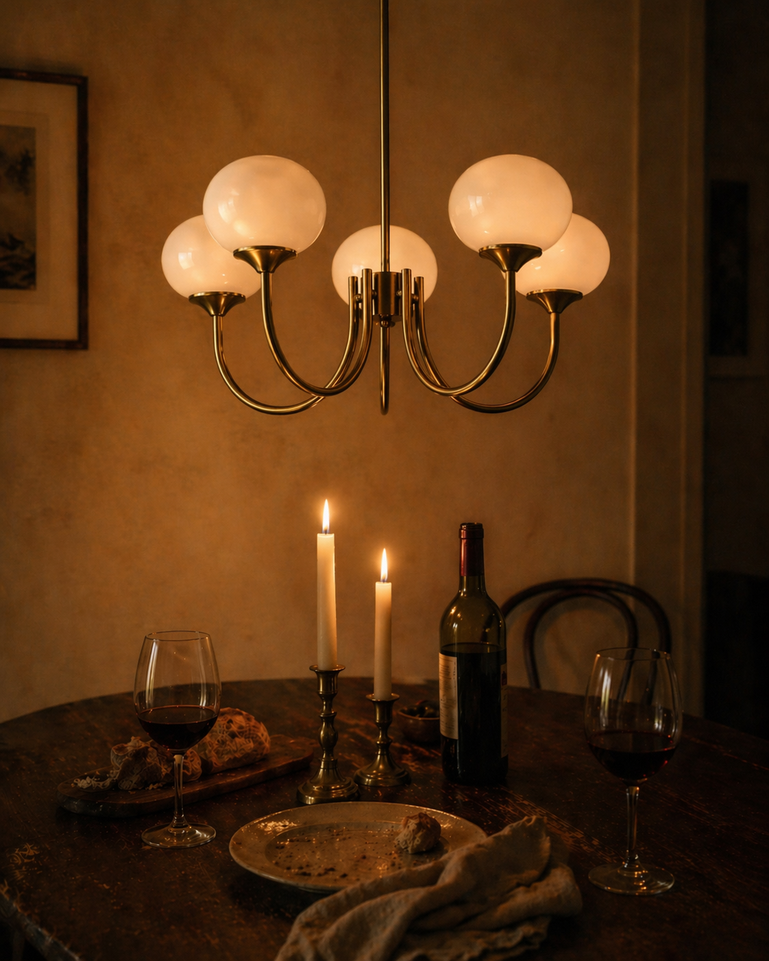 Pale chandelier over a wooden dining table with candles and wine