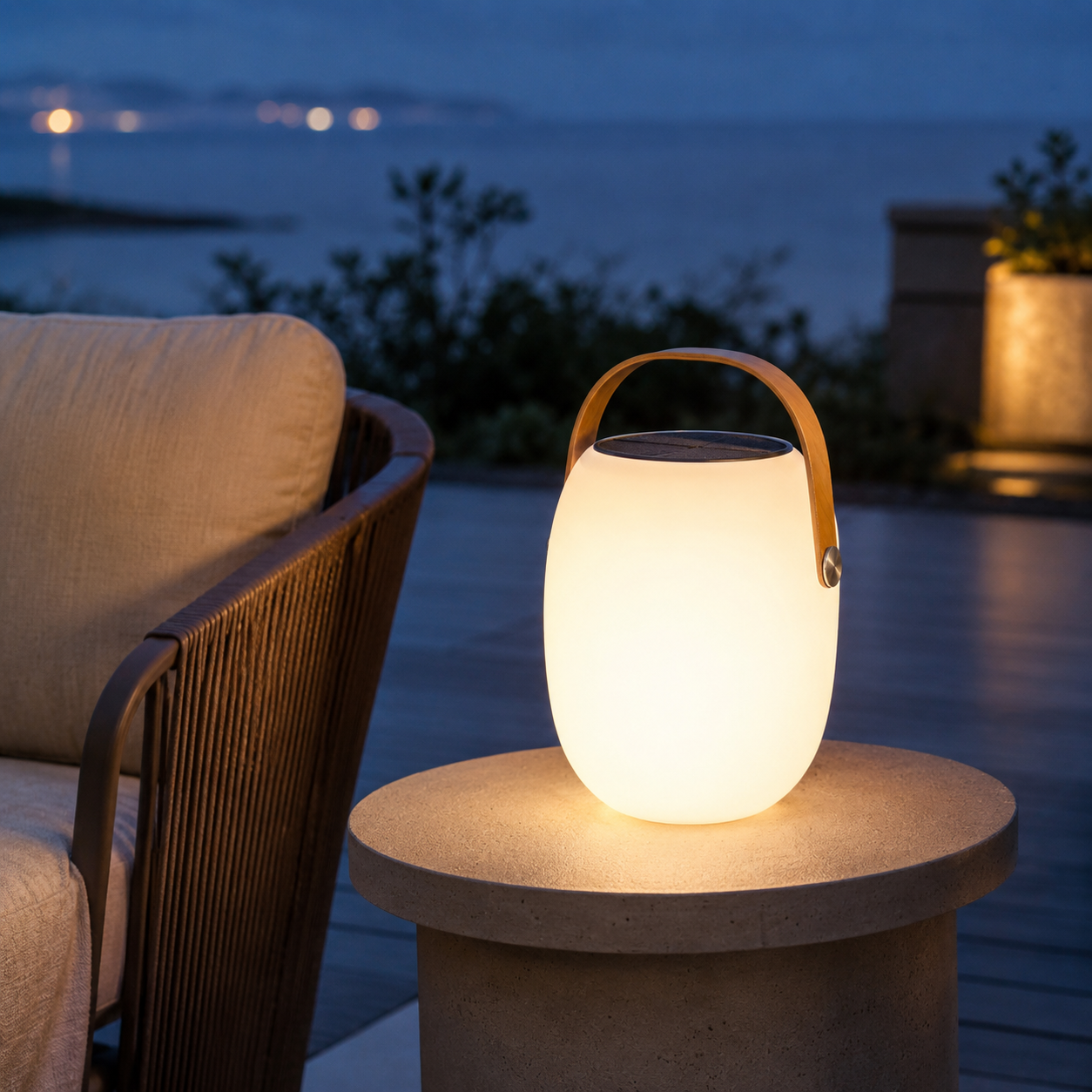 Aire portable outdoor lantern on stone side table on terrace overlooking water and city lights at dusk