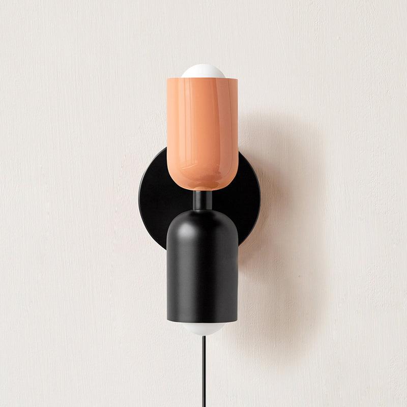 Alvor wall sconce with pink upper and black lower painted metal shades on a plaster wall