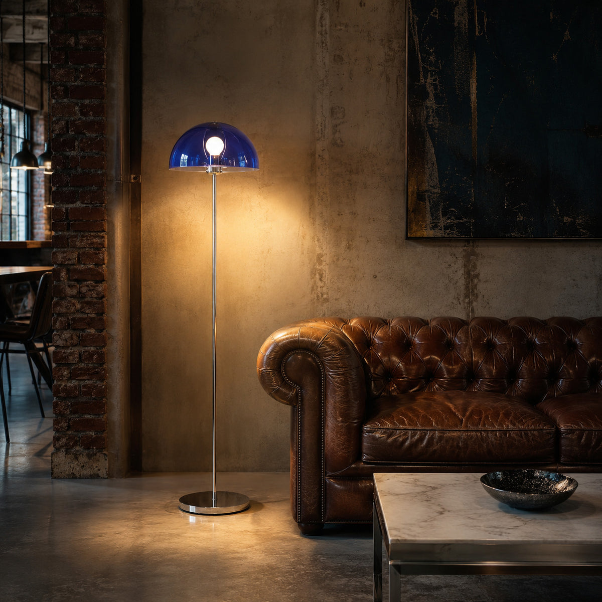 Benavente floor lamp with a cobalt inner dome, lit beside a leather sofa against brick