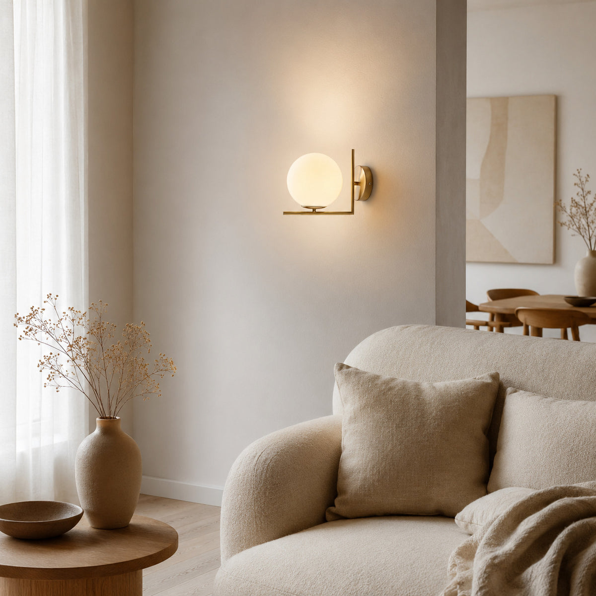 Ceira globe wall sconce in brass, lit beside a boucle sofa in a pale living room