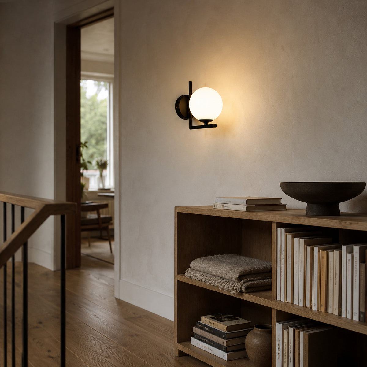 Ceira globe wall sconce in matte black, lit beside open shelving with books and bowls