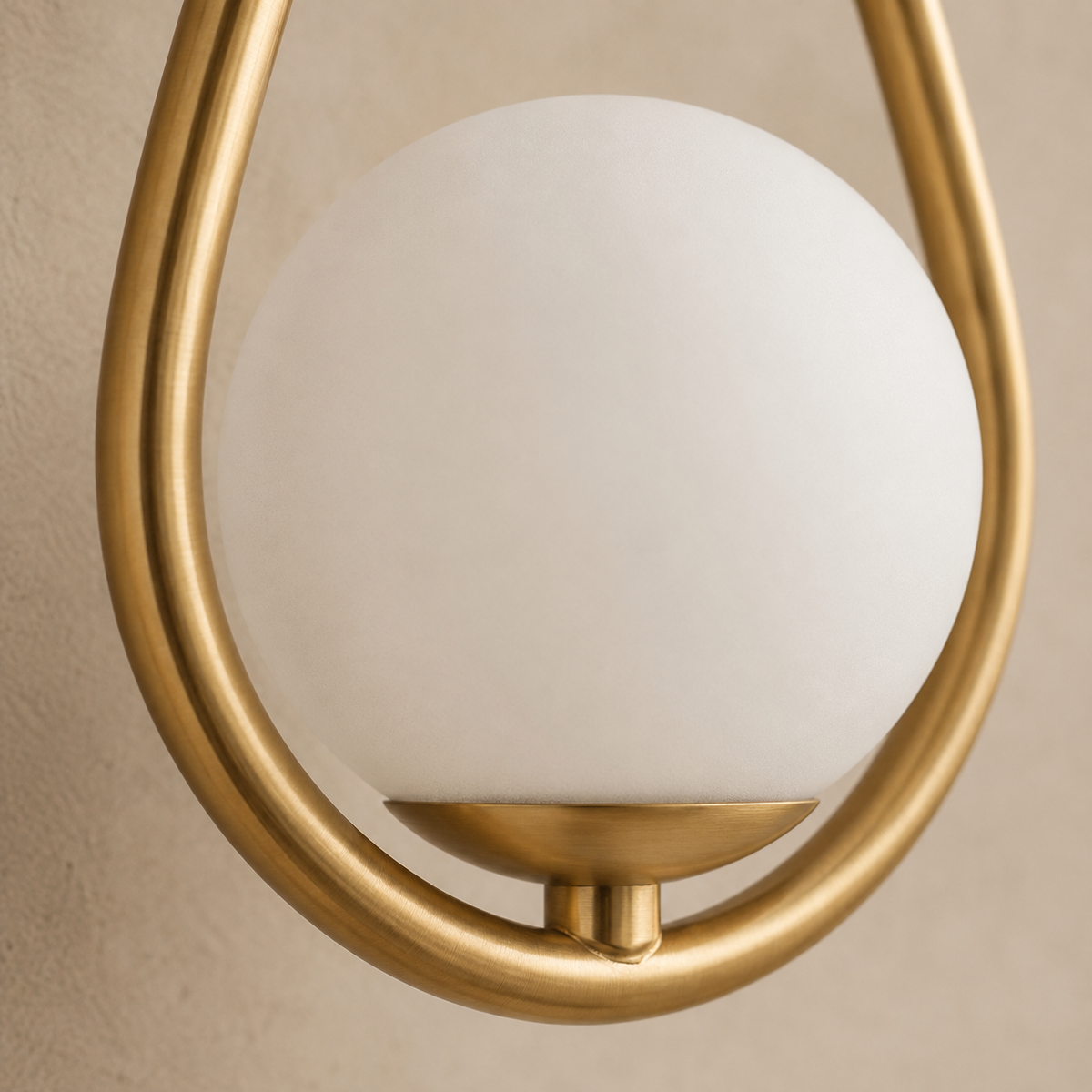 Frosted opal glass globe resting in the brass loop cradle of the Celorico sconce.