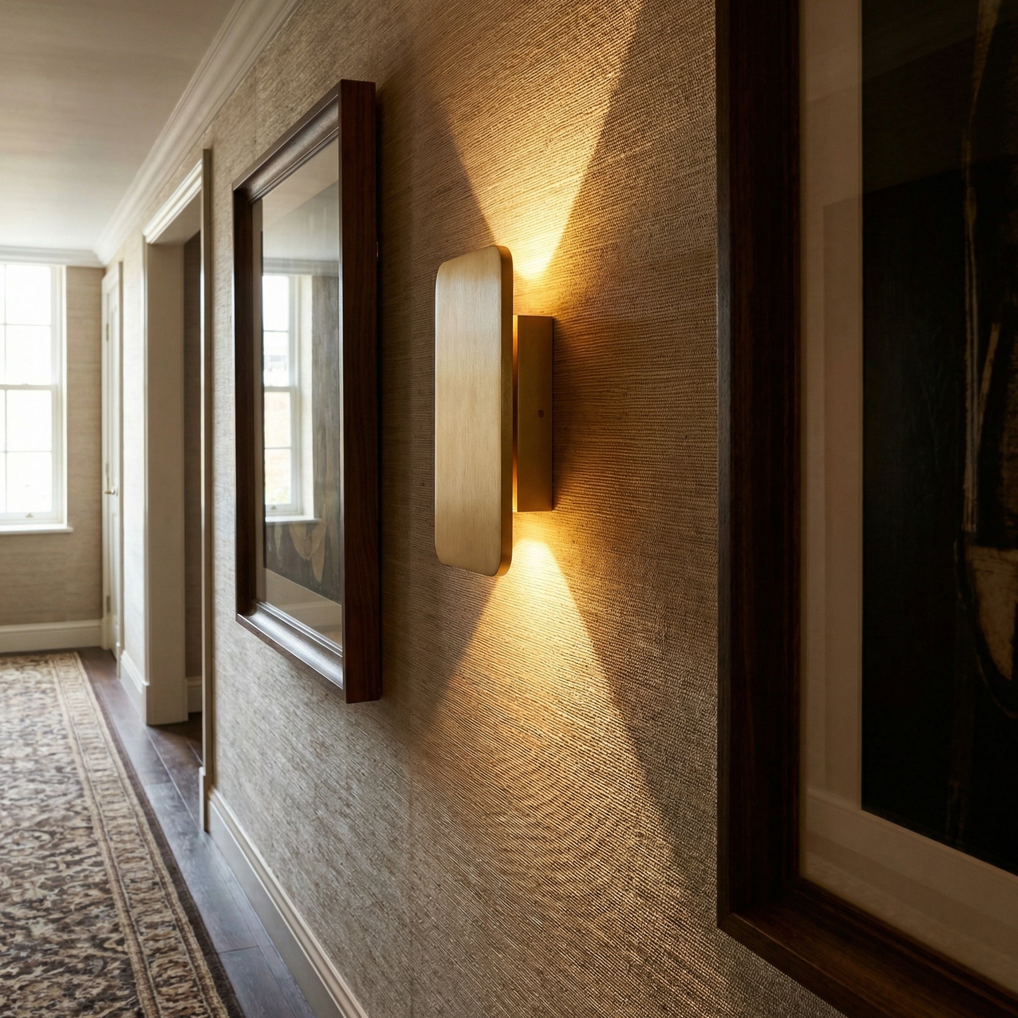 Guarda. wall sconce in gold on textured hallway wall beside a framed mirror, warm glow