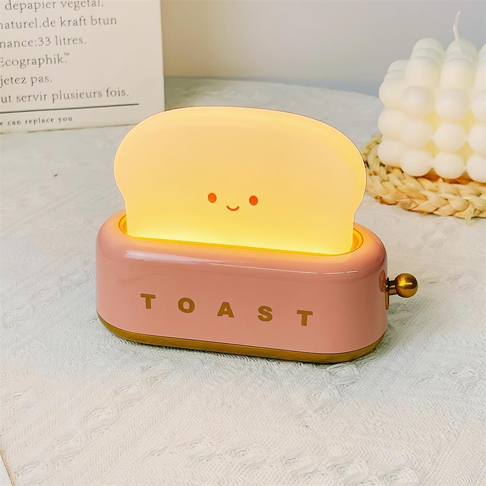 Portable toaster-shape LED night light in pink with smiling toast face, product shot.
