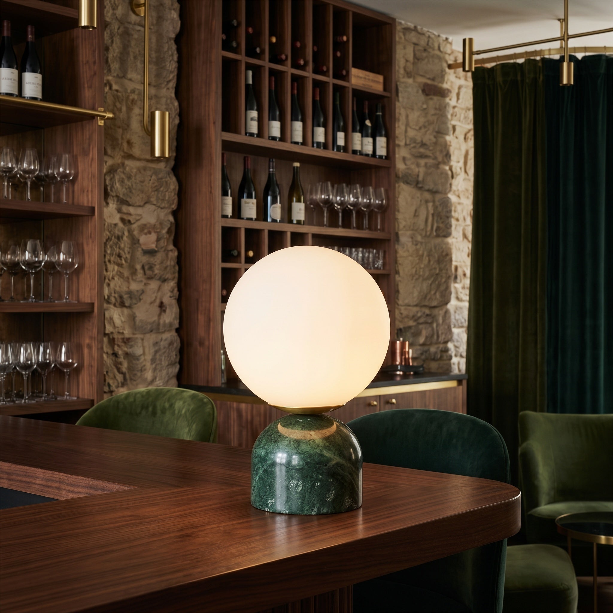 Green marble table lamp on a wood bar with green velvet chairs and wine shelves.