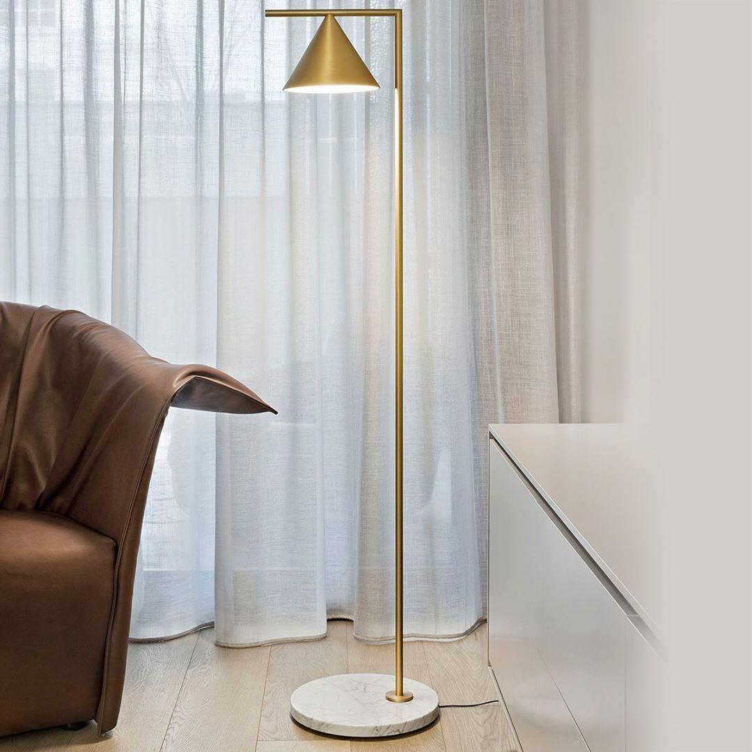 Copper cone floor lamp beside curtains and a brown leather armchair.