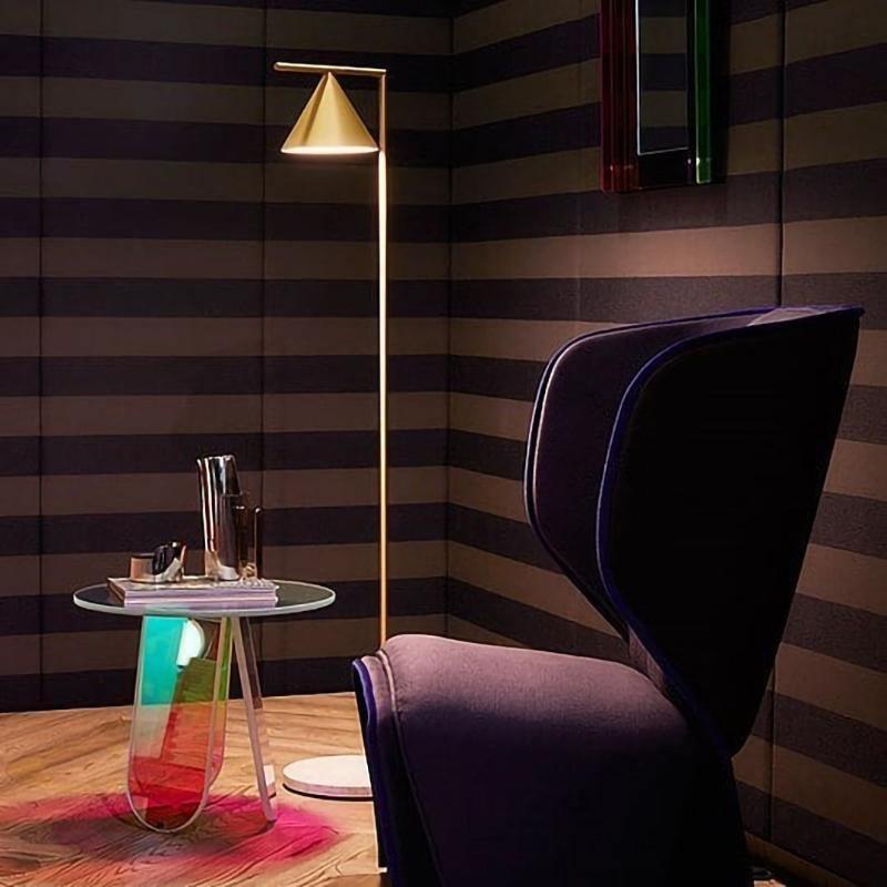 Copper cone floor lamp by a striped wall with a dark armchair and glass table.