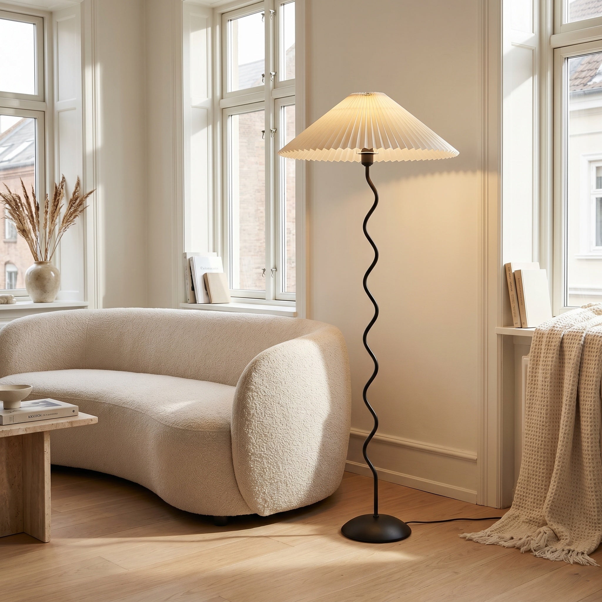 Wavy-stem floor lamp with white shade beside a curved boucle sofa in a bright living room.