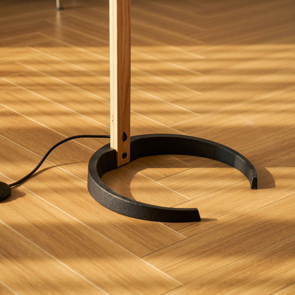 Cast-iron crescent base bolted to the beech stem on sun-striped wood flooring.